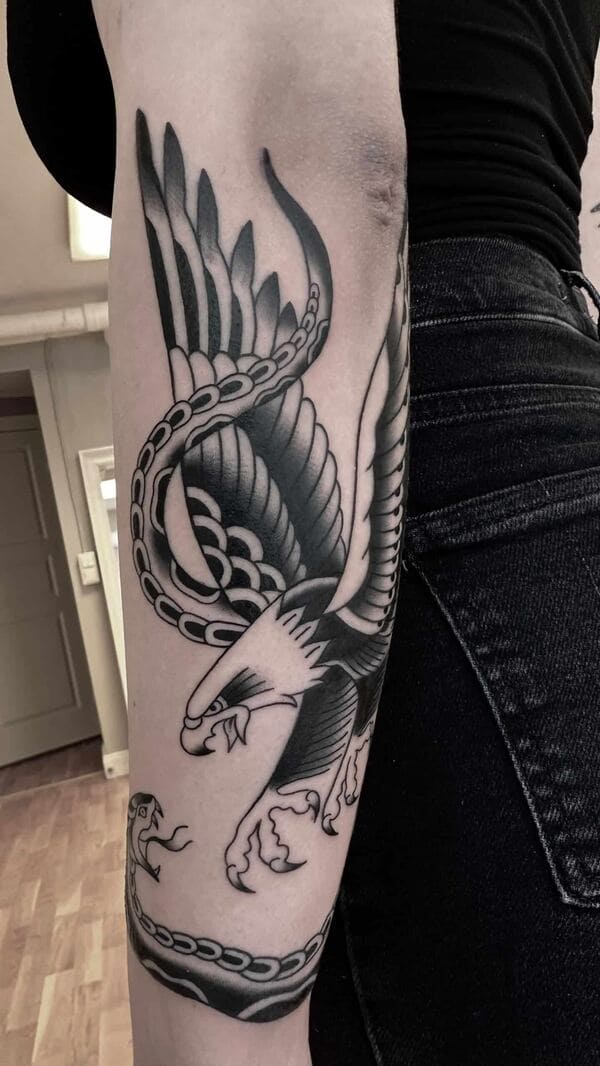 blackwork tattoo on an arm, of a snake and eagle looking at eachother with open mouths.