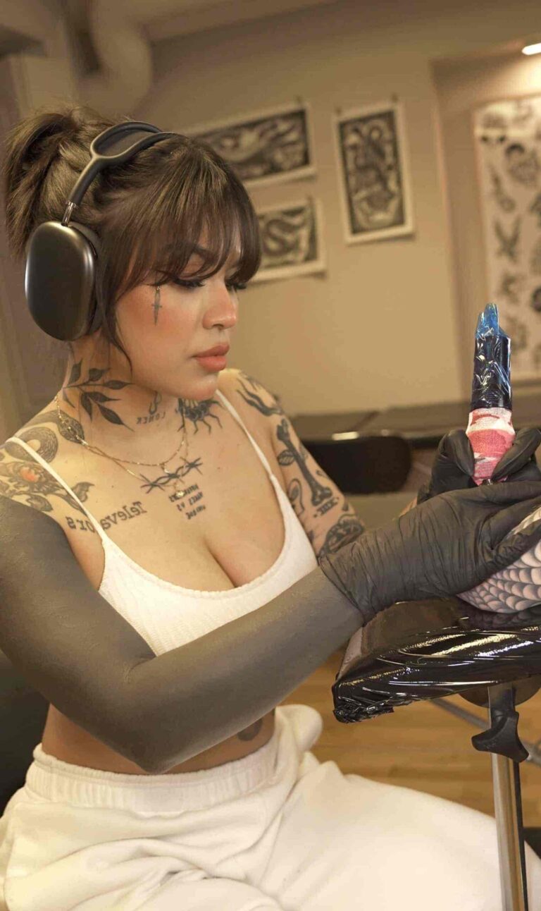 Tattoo artist sitting with headphones on and holding a tattoo pen.