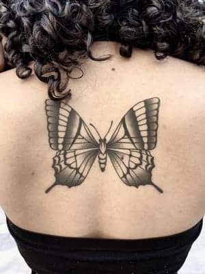 Healed tattoo on a womans back of a black butterfly.