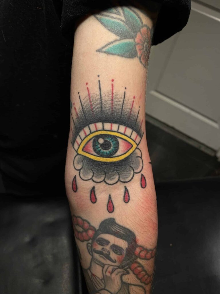 Healed tattoo on an arm of a blue eye with red drops under it.