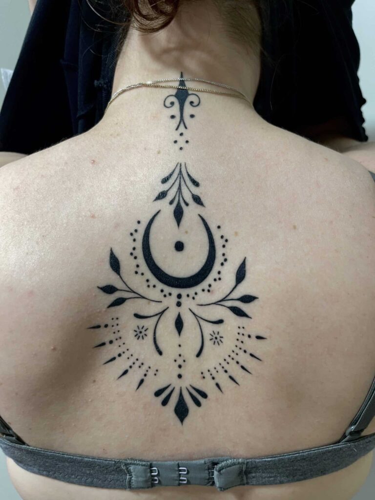 Healed tattoo on a womans back of ornamental crescent moon.