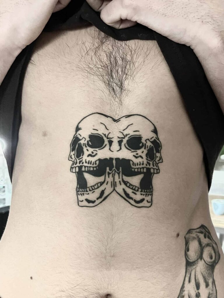 Healed tattoo of two skulls stuck together with open mouths.