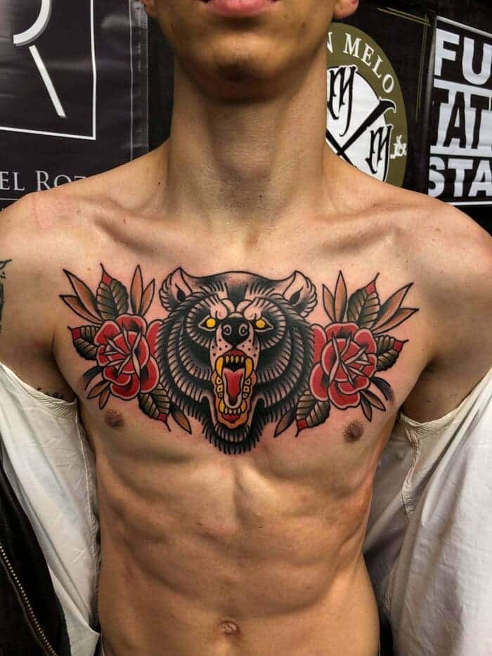 Traditional tattoo on a boys chest of a bear with an open mouth and two flowers next to it.