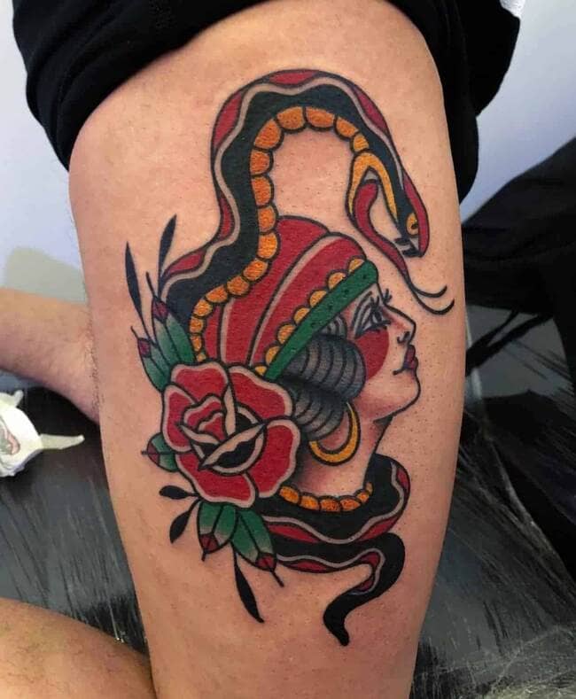 traditional tattoo on a leg of a girl with a snake on her head and a flower next to her.