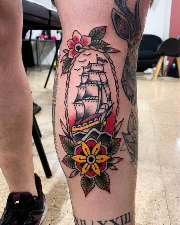 Traditional tattoo on a calf of a sailboat with a rope and flowers around it.