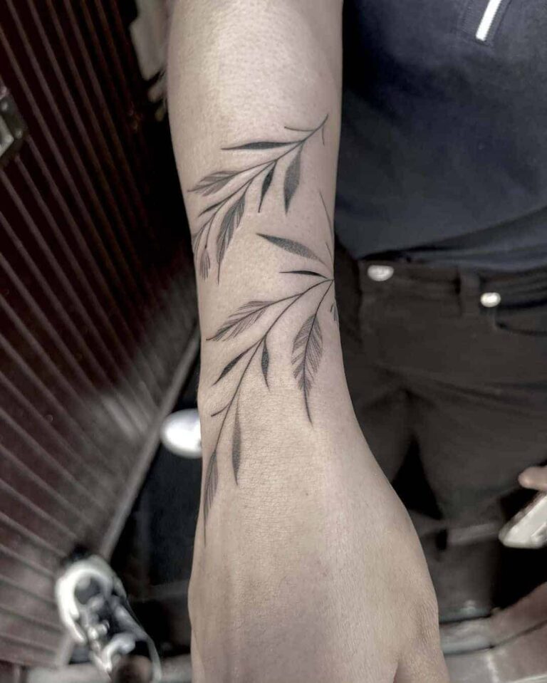 Fine line tattoo on a arm of two branches with leaves.