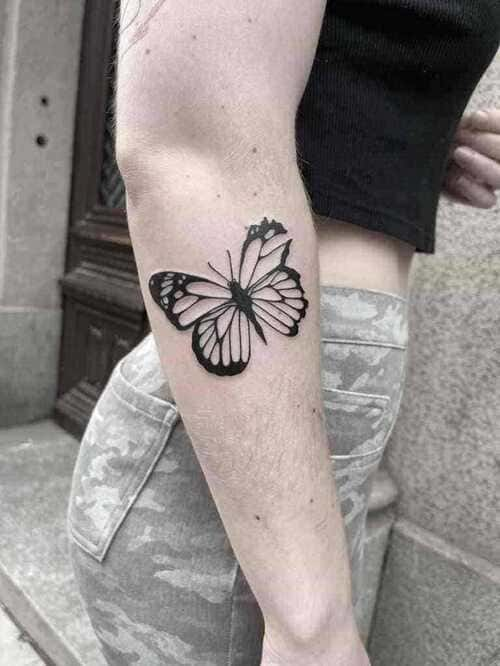 Minimalist tattoo of a black butterfly on a womans arm.