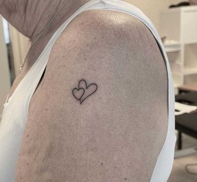 Minimalist tattoo of two hearts on a shoulder.