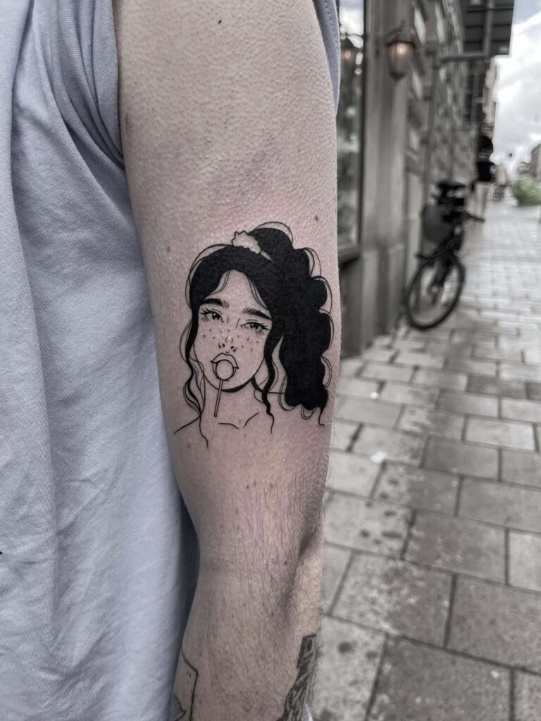 Svart tatuering av en tjej med fräknar och en klubba.